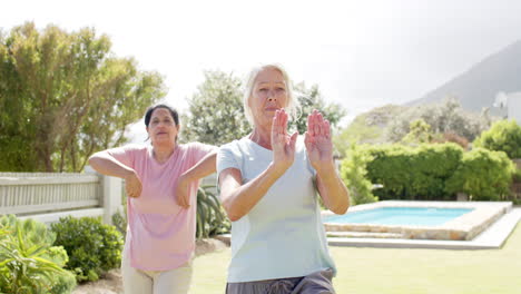 Two-focused-diverse-senior-women-practising-yoga-in-sunny-garden,-slow-motion,-copy-space