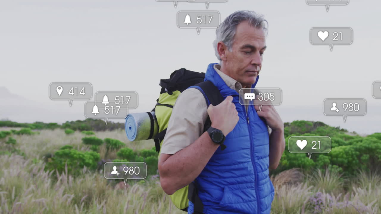 Mature hiker standing in field, carrying backpack, displaying floating social media marketing icons