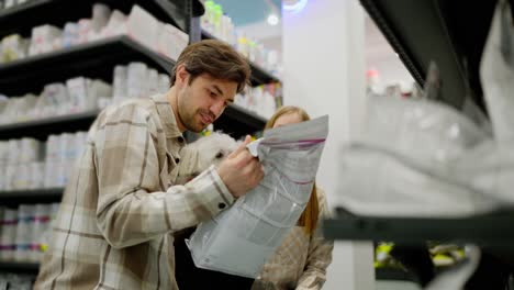 a happy couple a brunette guy and a blonde girl in checkered shirts together with their white dog inspect items in a pet store and choose the one they need