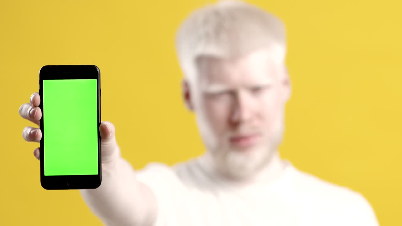 알비노 남자가 크로마 키 스크린과 노란색 배경을 가진 스마트폰을 보여줍니다.