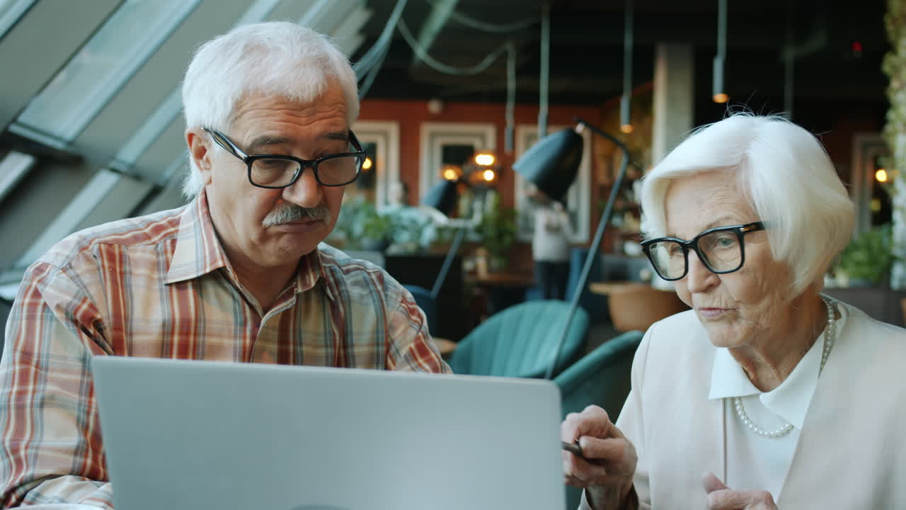 Elderly Couple Discussing on Laptop in Cafe