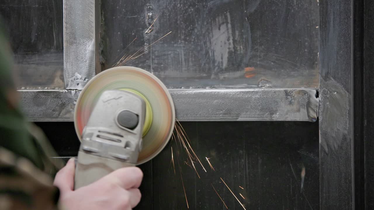 カウカシアの手で洗する 溶接された縫い目を 角磨き機で フラップディスクで 溶接した金属の構造に 長いスパーク・トレイルで クローズアップ スローモーション