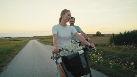 front view of cheerful caucasian couple of middle age riding a bike on sunset on village road.