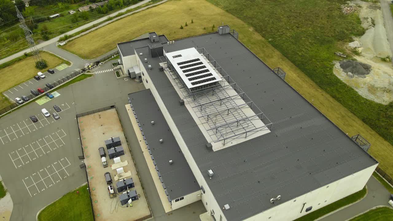 Aerial drone revealing video of a AI technology Data center in summer countryside with cooling systems fans spinning on the rooftop and parking lot in the front. Quantum computing in modern building
