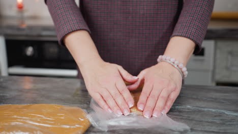 panadero presionando la masa dentro de una envoltura de cuero blanco en el mostrador de la cocina mientras otra masa descansa cerca, preparándose para hornear en un entorno de cocina moderno con iluminación cálida y espacio de trabajo limpio