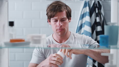 view through bathroom cabinet of young man taking medication from container