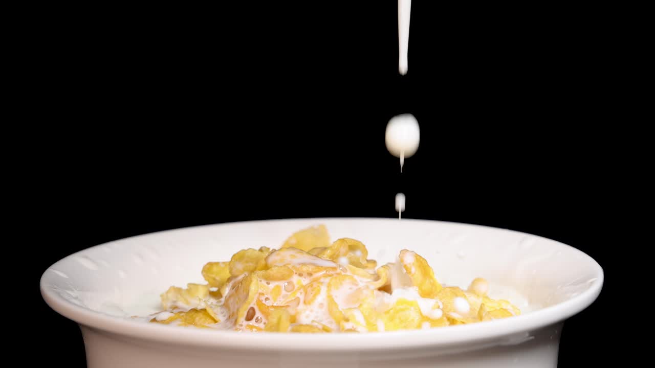 Milk streams into a bowl of corn cereal against a black backdrop, highlighting the contrast and motion
