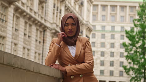 portrait of smiling muslim businesswoman wearing hijab and modern business suit standing outside city office buildings 7