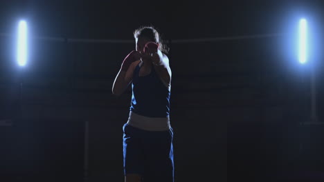 a beautiful sports boxer woman in red bandages on her hands and a blue t-shirt is fighting with a shadow practicing the speed and technique of punches. camera movement side view. steadicam shot. preparing for self-defense