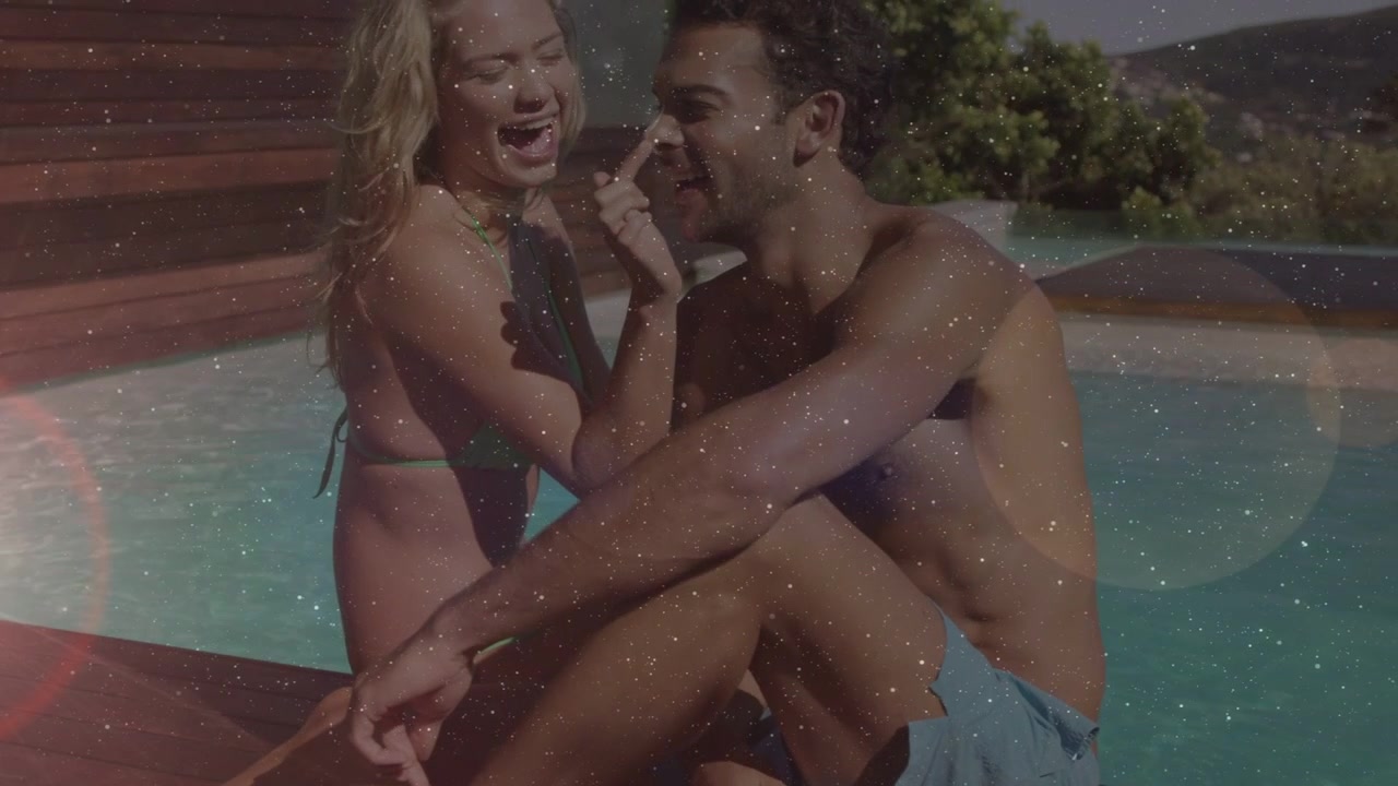 Couple sitting poolside laughing, camera pulling back revealing faces, flare overlay for marketing