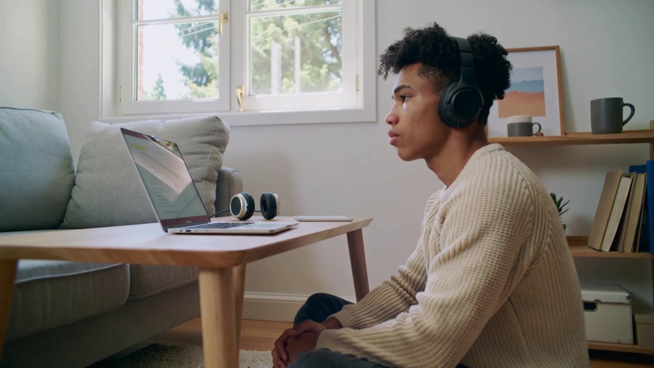 Studying man wearing cream-knit black headset on floor with open laptop and tablet, copy space