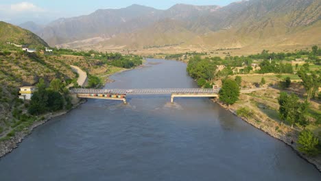 An-aerial-shot-of-a-bridge-crossing-a-river-in-a-green-village,-The-location-is-Kunar,-Afghanistan