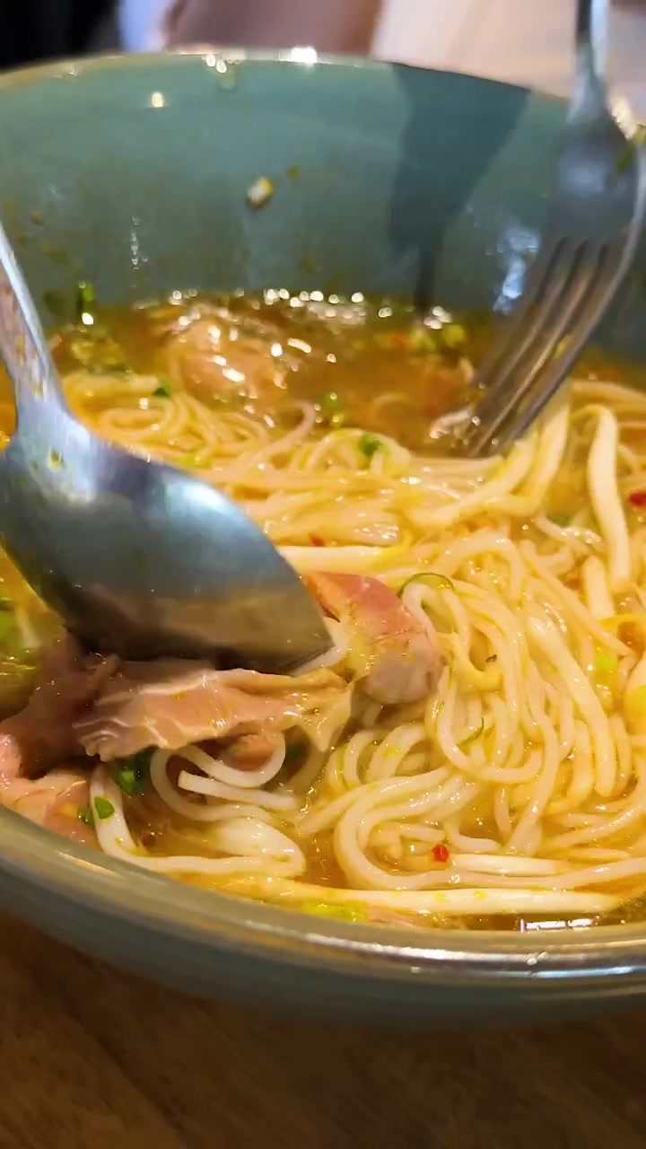 Una persona mescola e si prepara a mangiare una ciotola di pho vietnamita, evidenziando ingredienti vivaci e brodo ricco