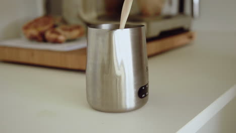 barista está vertiendo leche en una lata de leche metálica preparando un capuchino en casa en la cocina