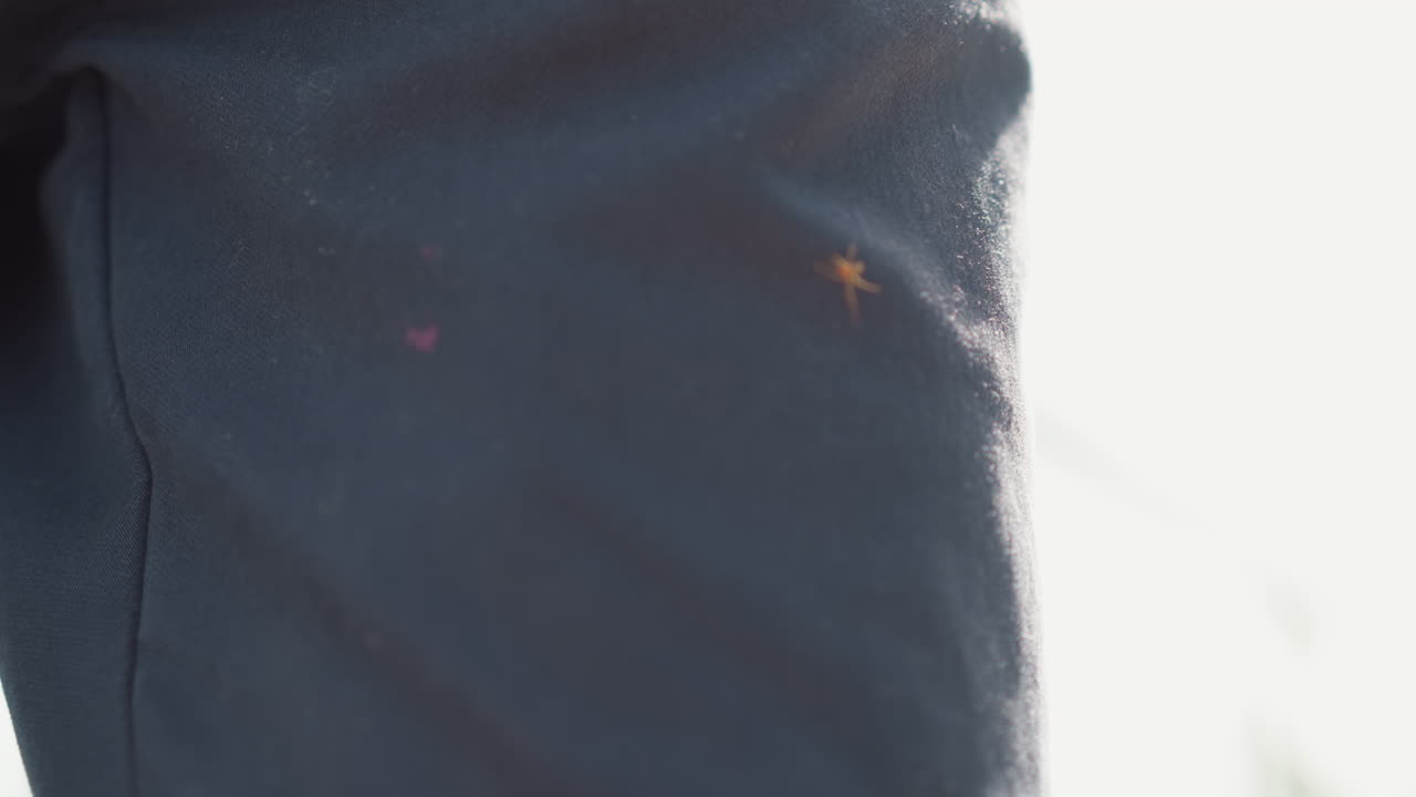 wet fabric sleeve with shimmering droplets and sunlight highlights closeup study of textile texture, visible seam and thread, subtle abrasion and wear after rain, quiet atmospheric clarity
