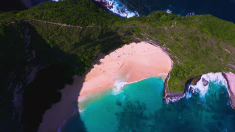 Sandy-Kelingking-beach-with-vacationing-people-below-green-cliff