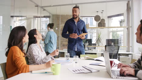 reunión de equipo de negocios creativo gerente de negocios presentando datos financieros a los accionistas usando tableta digital en una sala de juntas de oficina moderna casual con luz natural y grandes ventanas abiertas
