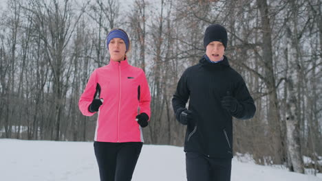 joven pareja familiar, hombre y mujer, corriendo por la mañana en el bosque de invierno. una mujer con una chaqueta holgada y un hombre con una chaqueta negra corre por un parque de invierno. estilo de vida saludable familia feliz
