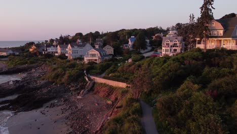 Aerial-sunset-of-Ogunquit-Maine-USA-drone-fly-above-waterfront-house-luxury-resort-revealing-Marginal-way-trail-path-on-Atlantic-Ocean-coastline