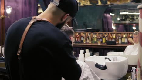 vista trasera de un barbero barbudo cortando el cabello usando un cortador eléctrico en el cuello de su cliente en la toma del barbero. toma en cámara lenta