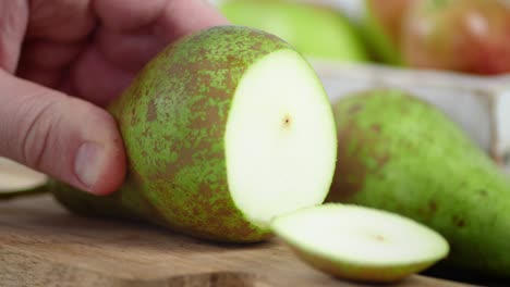 the hand of a man with a knife cut into round slices of pear.