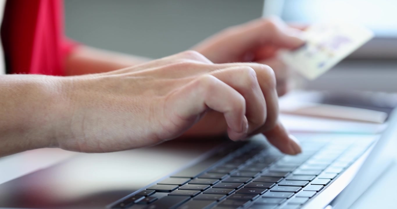 Woman types on laptop keyboard with hand holding credit card