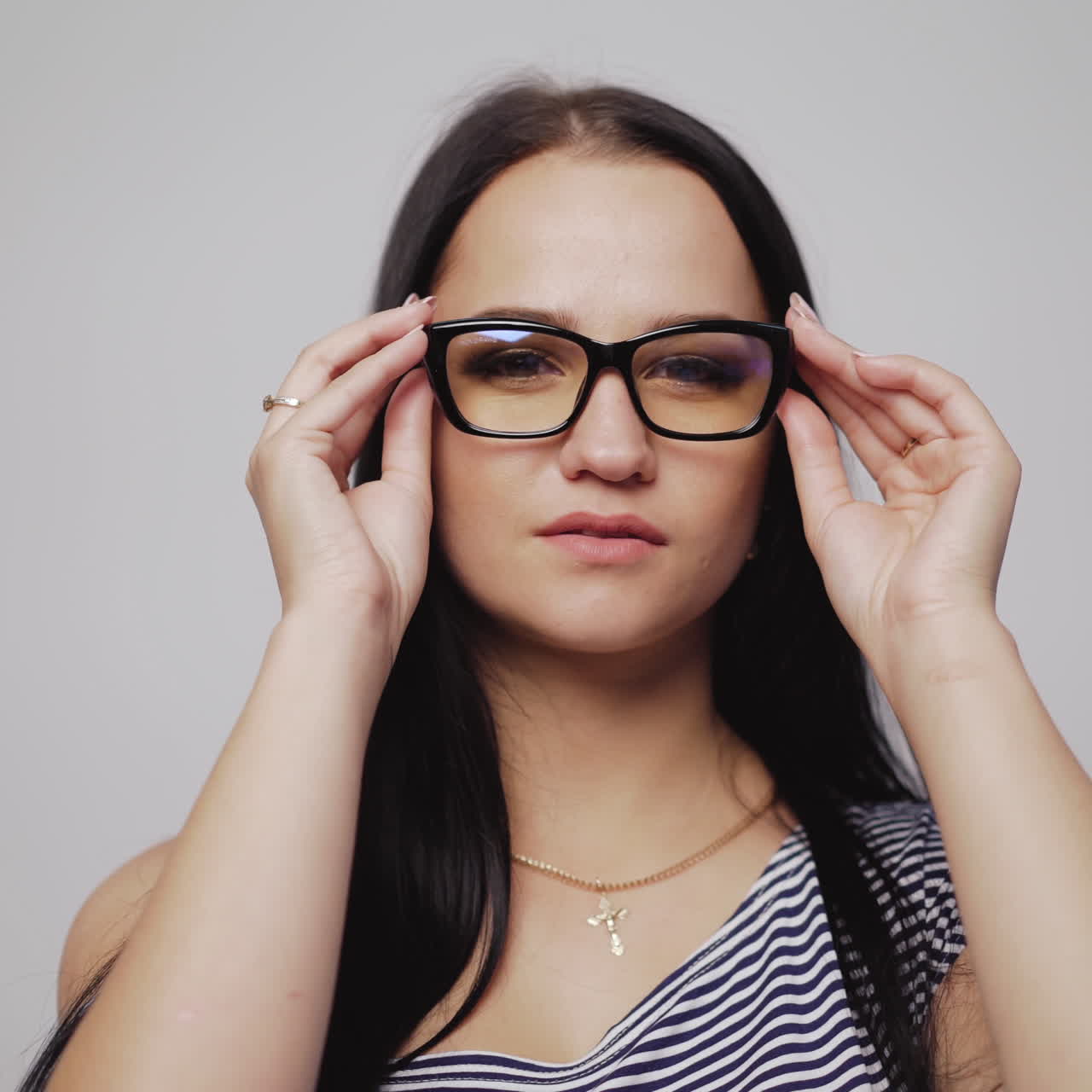 Serious young girl tries on fashionable eyeglasses in black rim over the light background. Attractive woman puts on new eyewear. Close-up