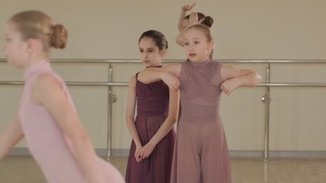 a group of young ballet students in black dancewear practicing positions in a spacious ballet studio with wooden flooring and wall-mounted barres. focused expressions and synchronized movements.