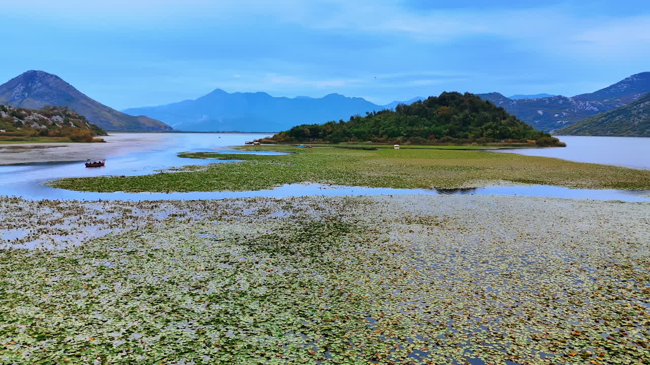 Vast waterscape covered with lotuses. Approaching the boats standing on the anchor near the little rocky islands
