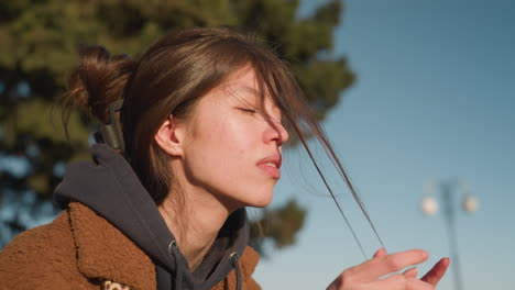 a close-up of a girl wearing a brown coat, looking deeply disturbed and anxious as she pulls at her hair. her expression reflects inner turmoil and distress, set against a clear sky background