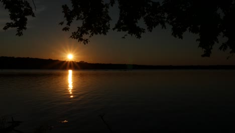 steady shot of a setting sun with reflections in a lake