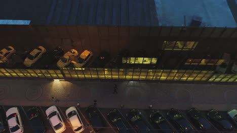 4k outside view of business district building , mall with wall mirror windows at evening or night .  reflection of city , people , cars in mirrored walls . drone camera moving . people working inside