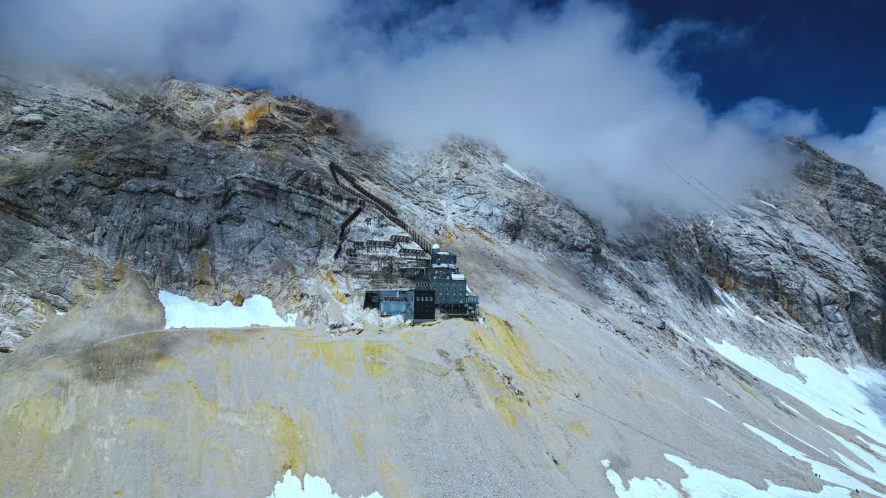 vista aérea de la montaña zugspitze, el pico más alto de alemania, con nieve esporádica, cielo azul y nubes en el fondo