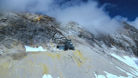 Luftaufnahme-Der-Zugspitze,-Dem-Höchsten-Gipfel-Deutschlands,-Mit-Sporadischem-Schnee,-Blauem-Himmel-Und-Wolken-Im-Hintergrund