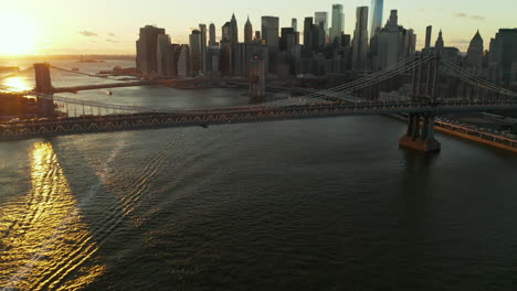 Amazing-footage-of-large-suspension-bridges-over-river-in-sunset-time.-Tilt-up-reveal-of-skyline-with-modern-tall-skyscrapers.-Manhattan,-New-York-City,-USA