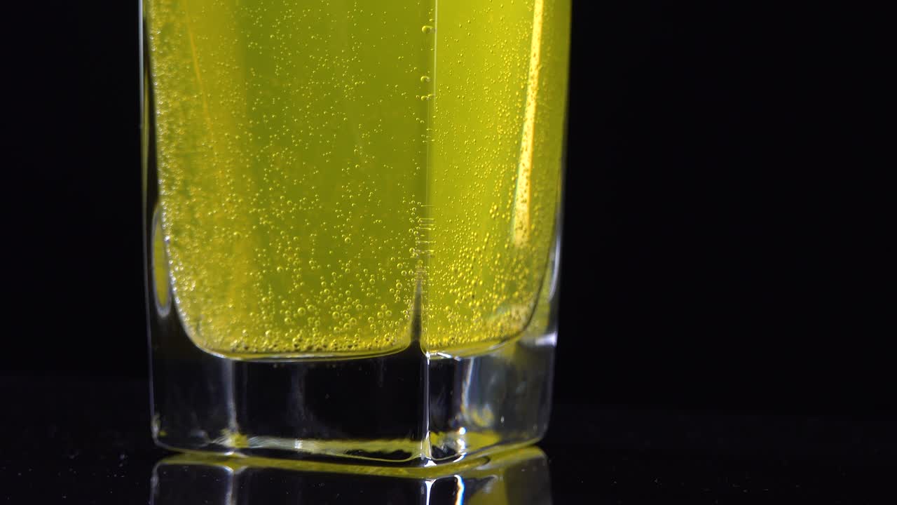 cerca de la tableta de vitamina c disuelta en un vaso de agua mineral fresca en un fondo oscuro. tiro macro de líquido burbujeante amarillo con bolas de oxígeno