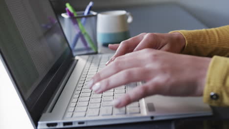 Midsection-of-biracial-woman-sitting-at-desk-using-laptop-at-home,-slow-motion