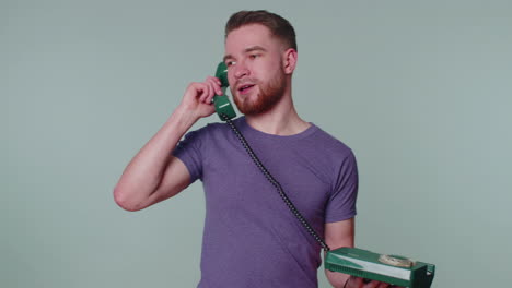 crazy sincere young man talking on wired vintage telephone of 80s, fooling, making silly funny faces
