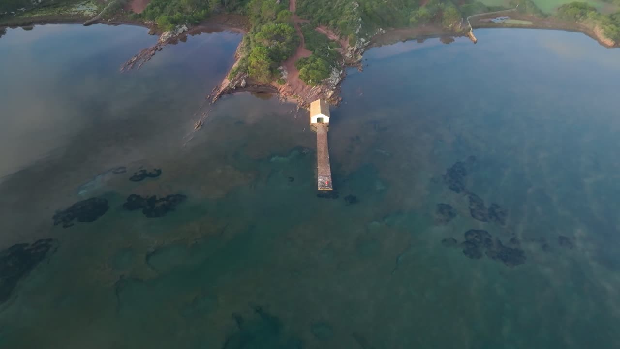 drone aéreo arriba abajo casa de muelle en el océano azul paisaje de la isla verde menorca fornells bahía establecimiento de tiro