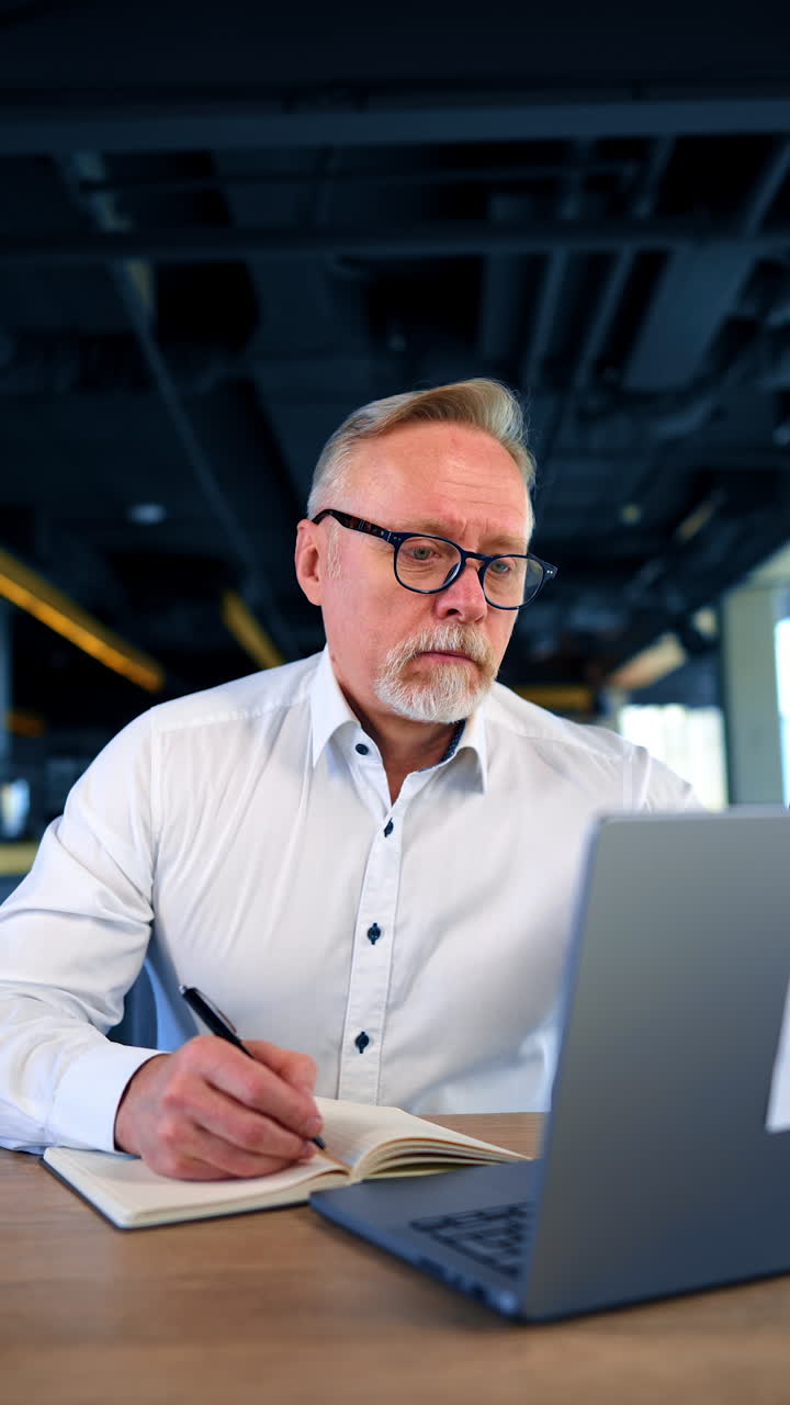 Caucasian businessman works in the office. Man looks at computer screen, puts his pen and leans back in his chair. Vertical video.