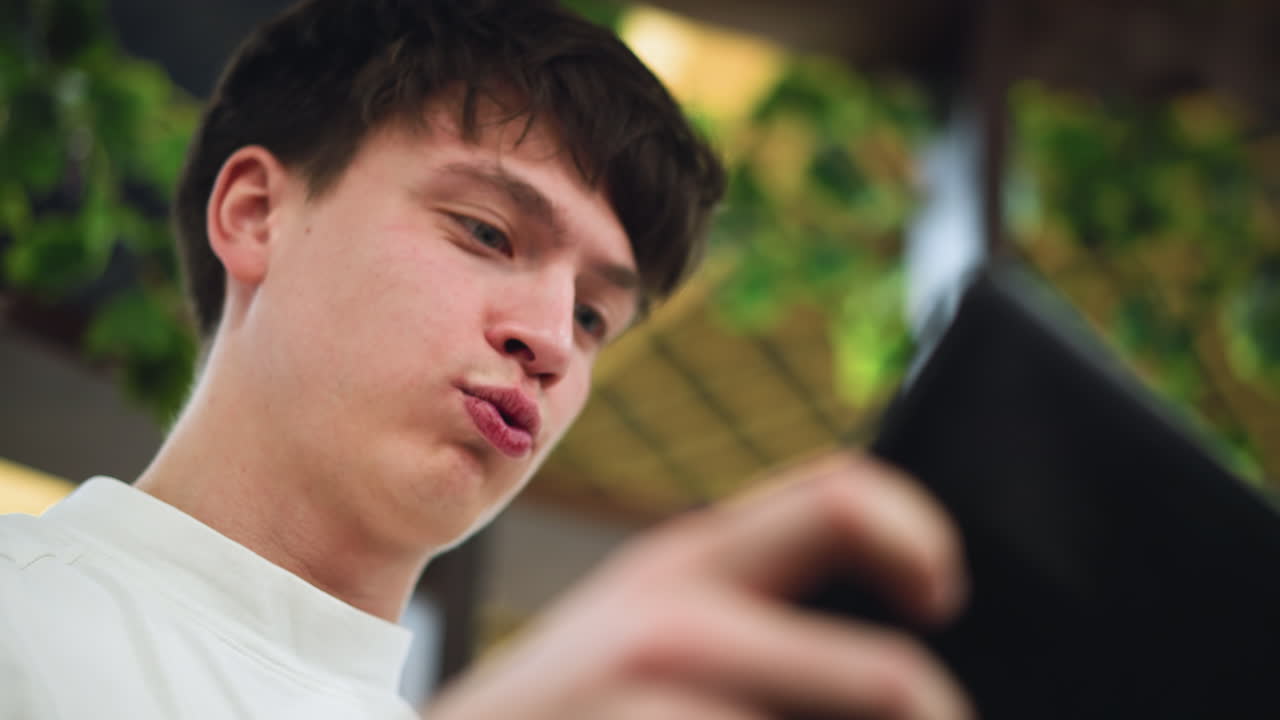 Close head view very fair young lad smiling while playing game on phone screen capturing joyful expression light glint on face conveying playful youthful immersion in mobile entertainment moment