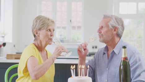 retired couple celebrating birthday with glass of champagne and cake at home together