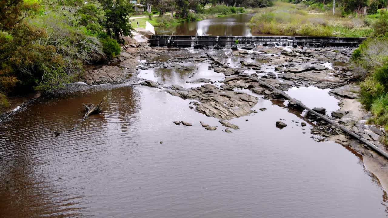 grabación de video aéreo a través de la presa con agua corriendo entre las rocas por el arroyo