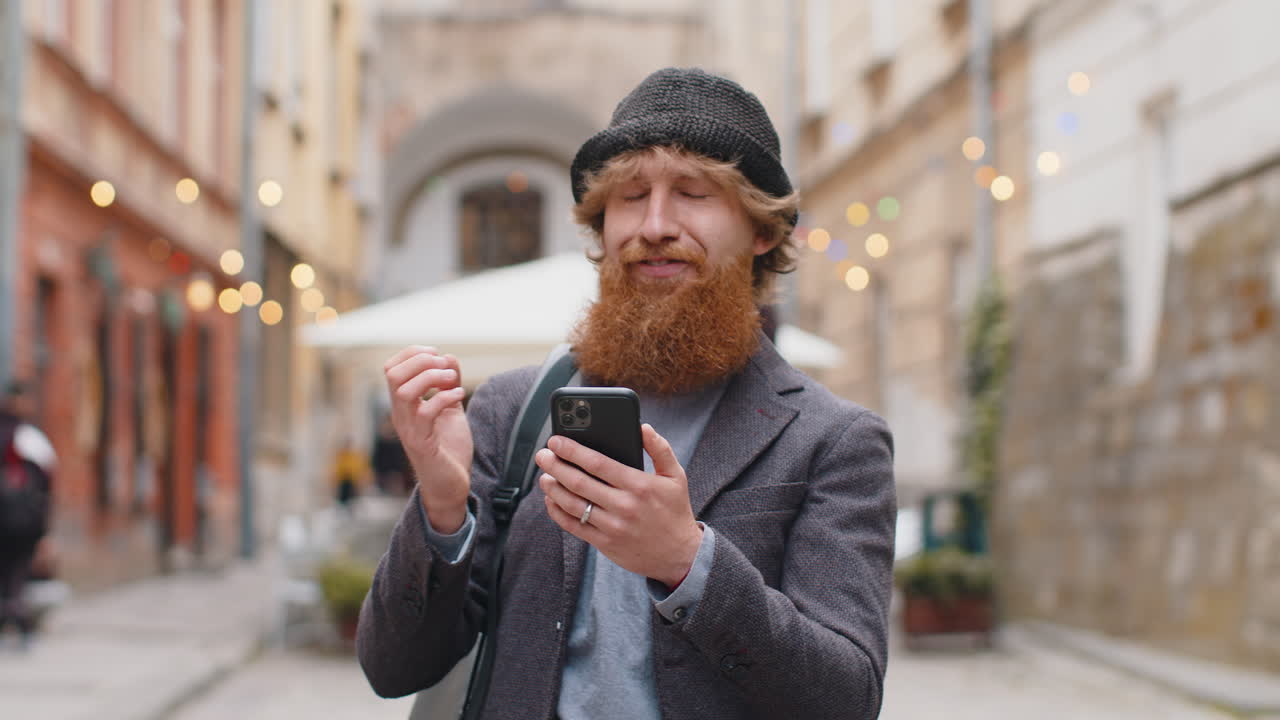 Excited happy winner young man use smartphone celebrating win good message news in city street