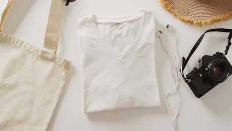 video of close up of white t-shirt, bag, sunhat, earphones and camera on white background