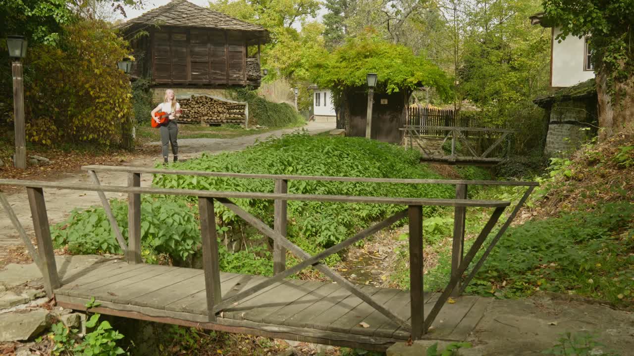 mujer músico de buen humor baila en la calle de un pueblo tradicional búlgaro