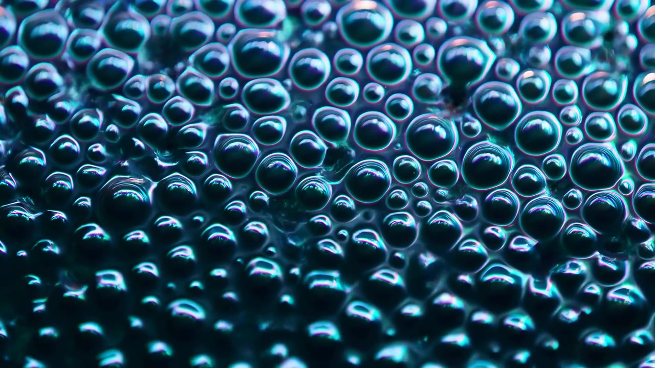 Un gros plan de bulles denses et brillantes couvrant la majeure partie de l'image, l'amas principal étant concentré au centre supérieur et dans la moitié supérieure. Tons sarcelle, cyan et bleu.