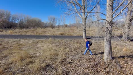 mature man wearing a backpack walking in a field and between trees - aerial view in slow motion