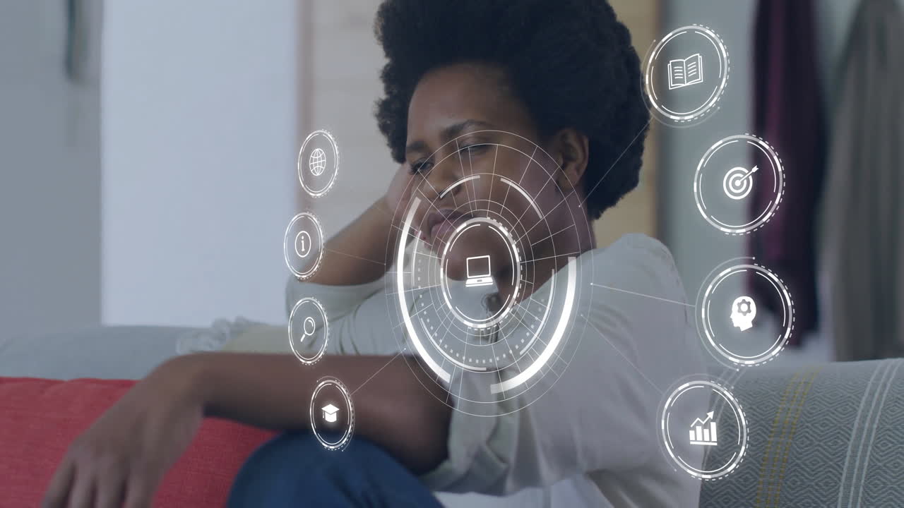 Relaxing on couch, African descent woman interacting with digital animation icons