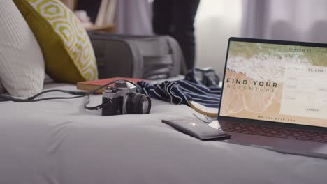 person packing suitcase for summer holiday with laptop showing booking details of flights and hotel in foreground